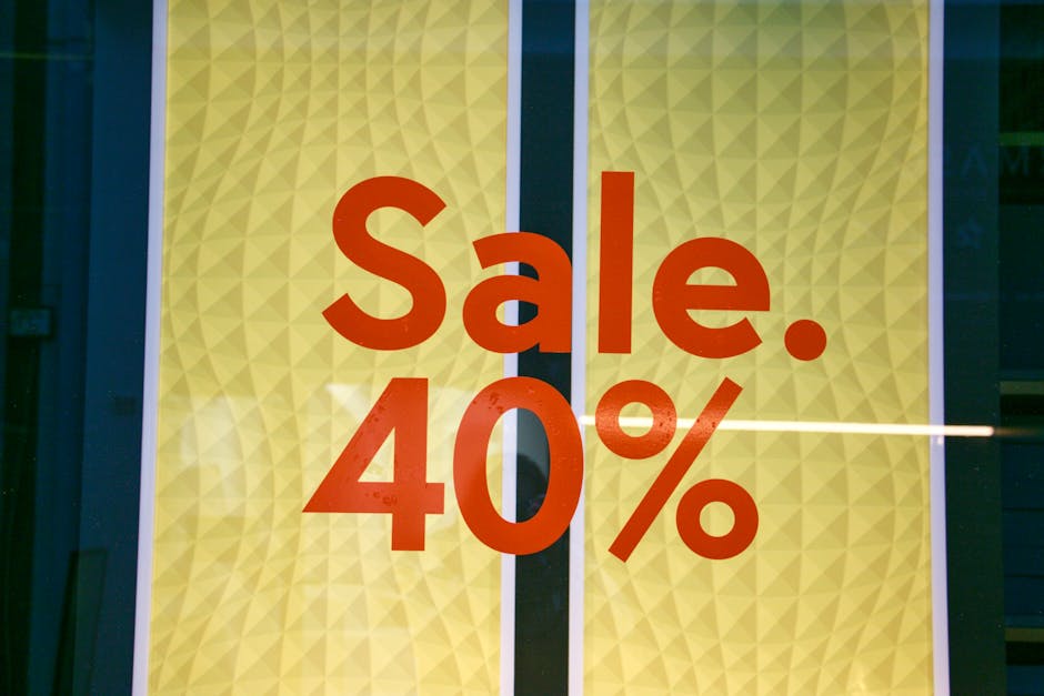Close-up of a glass window storefront displaying a bright yellow patterned background with bold red text indicating a 'Sale. 40%' discount, likely for a flower shop or floral arrangement sale event, w