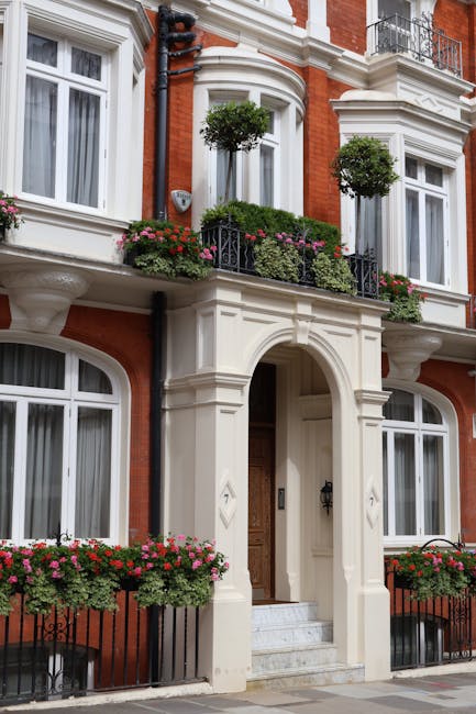 A detailed exterior view of a red-brick townhouse with white decorative stone accents, including arched windows and ornate columns framing the entrance. The building features a small balcony with blac